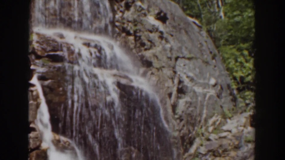 The 8mm frame holds on frothy water spilling down a steep rock surface, with foliage partly visible at the right edge.
