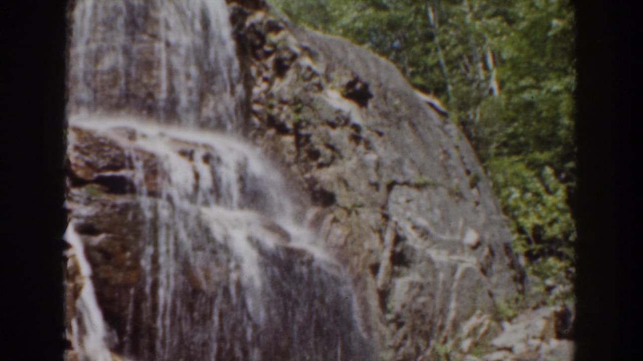 Final 1939 Mount Washington frame of a waterfall flowing across rugged rock, with green trees framing the upper and side edges.