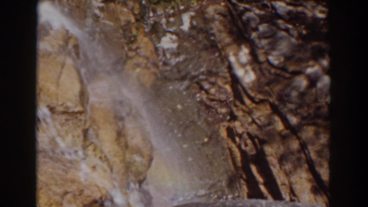 Mount Washington home-movie frame with a narrow white cascade over tan rock and darker fractured stone.