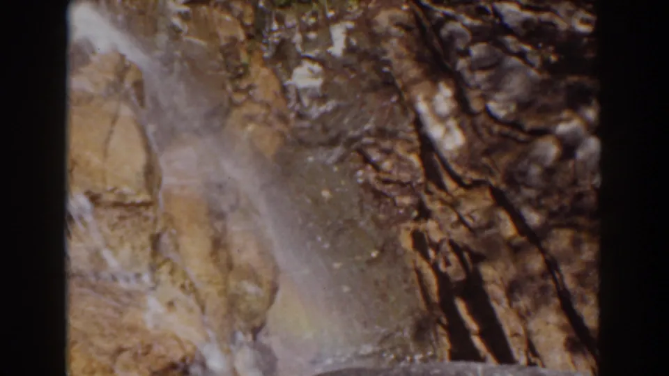 Mount Washington home-movie frame with a narrow white cascade over tan rock and darker fractured stone.