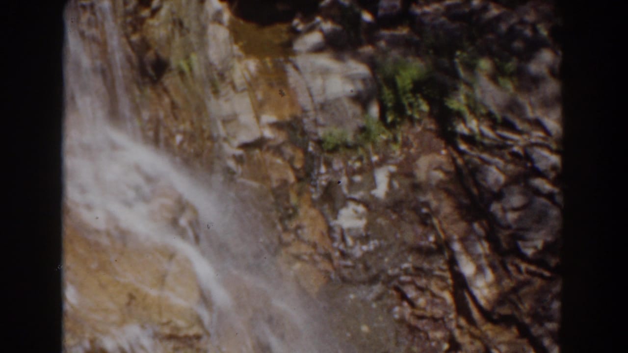 Mount Washington frame showing water moving over rock beside dark crevices and small green patches of vegetation.