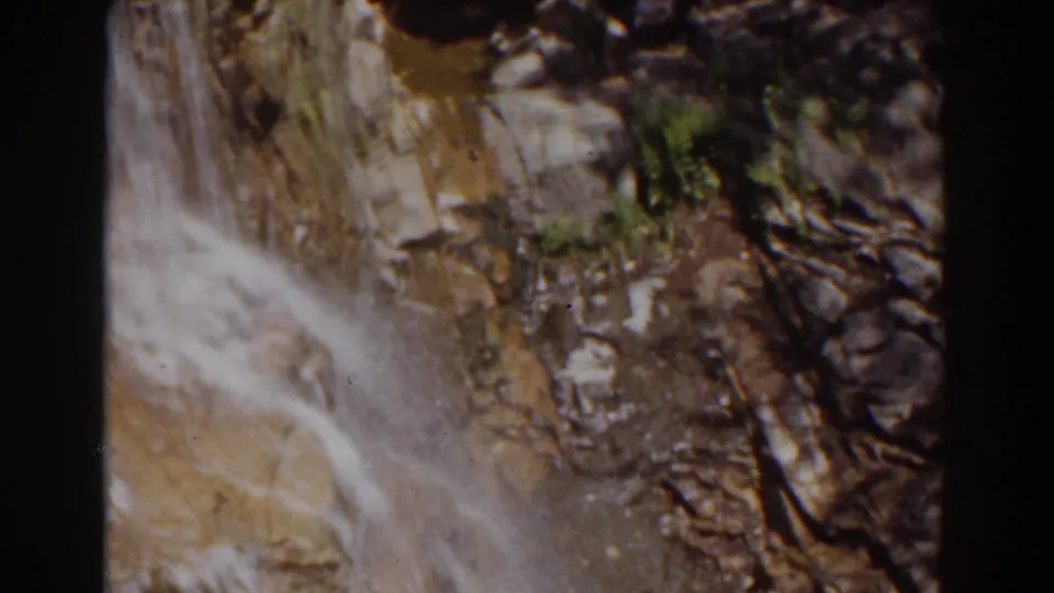 Mount Washington frame showing water moving over rock beside dark crevices and small green patches of vegetation.