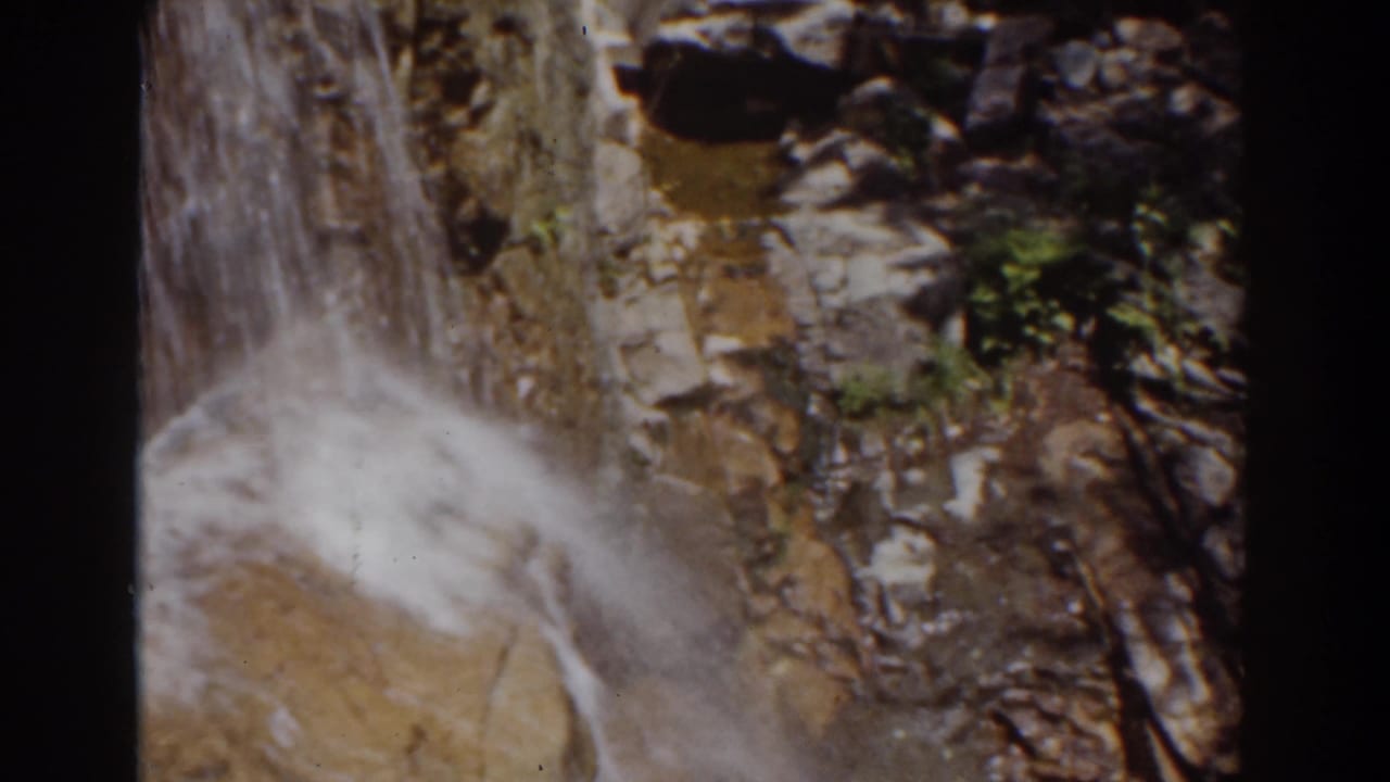 1939 8mm Mount Washington footage showing water falling over layered rocks with soft spray and dark film borders.
