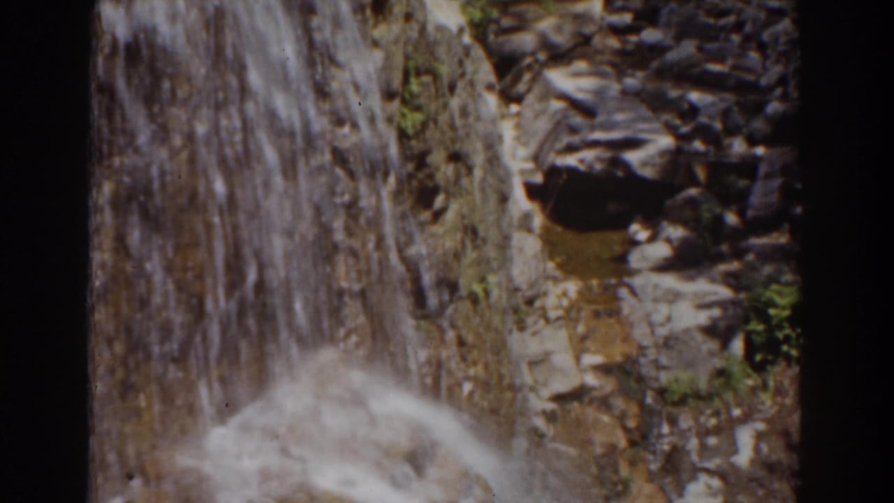 Close 8mm view of a Mount Washington cascade, with water running over brown and gray stone and a soft splash below.