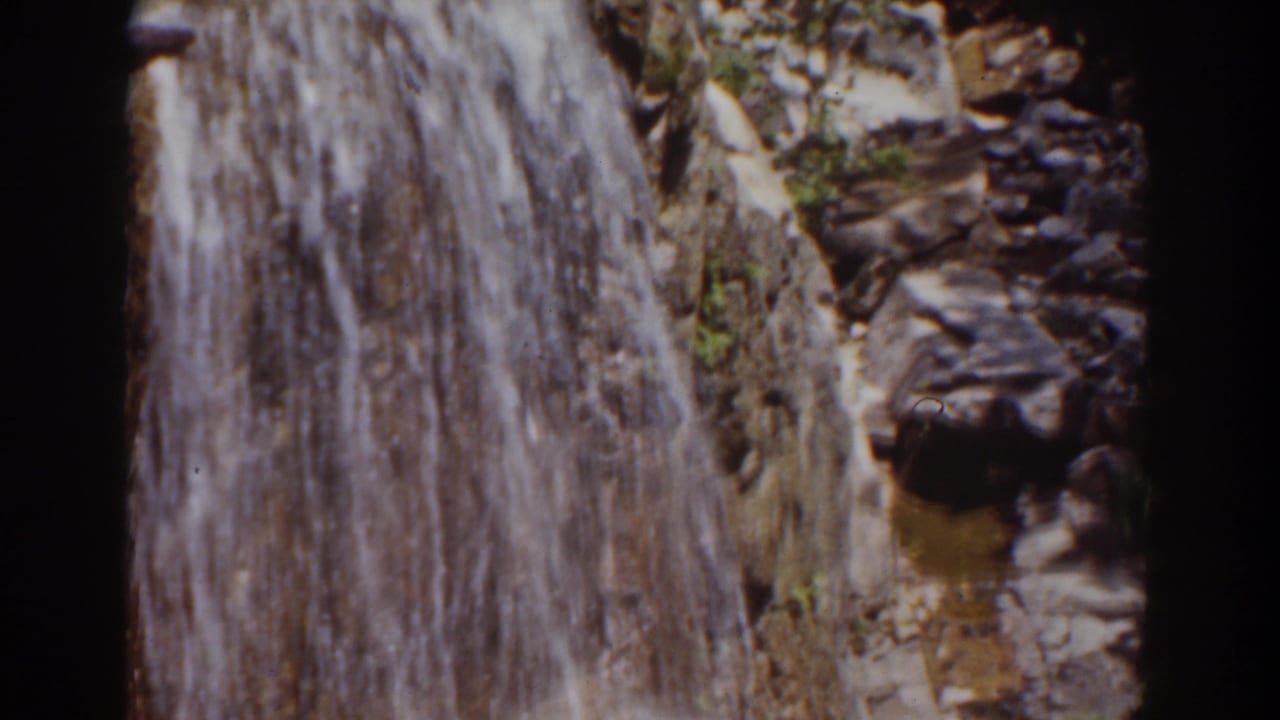 1939 home-movie frame of water dropping along a rocky Mount Washington cliff with scattered vegetation at the edge.