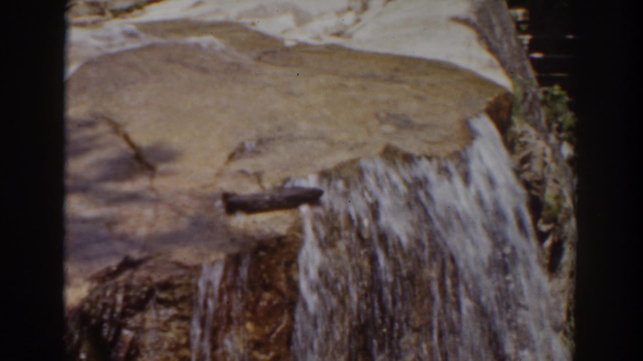 Water cascades over smooth rocks beside dark film-edge borders.