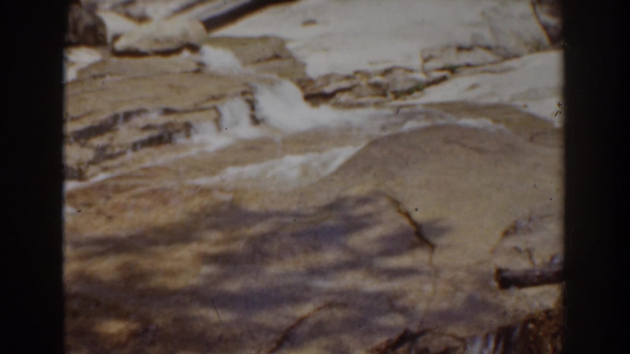 Archival 8mm view near Mount Washington shows white water moving across broad pale rock with a small dark log-like shape at right.