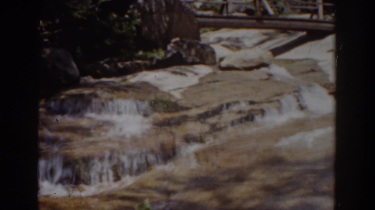Water flows over flat rock ledges beneath a wooden bridge railing.