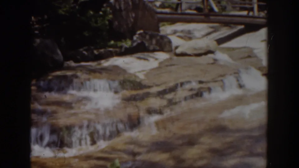 1939 Mount Washington-area 8mm frame showing a shallow cascade running over pale rock ledges below a wooden bridge railing.