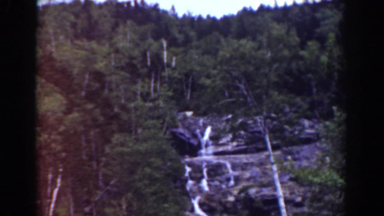 1939 Mount Washington home-movie frame showing a small waterfall dropping over rock ledges in dense forest.