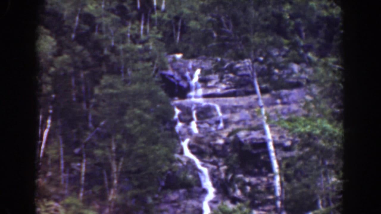 Tall cascade descending over a rocky cliff in forest.