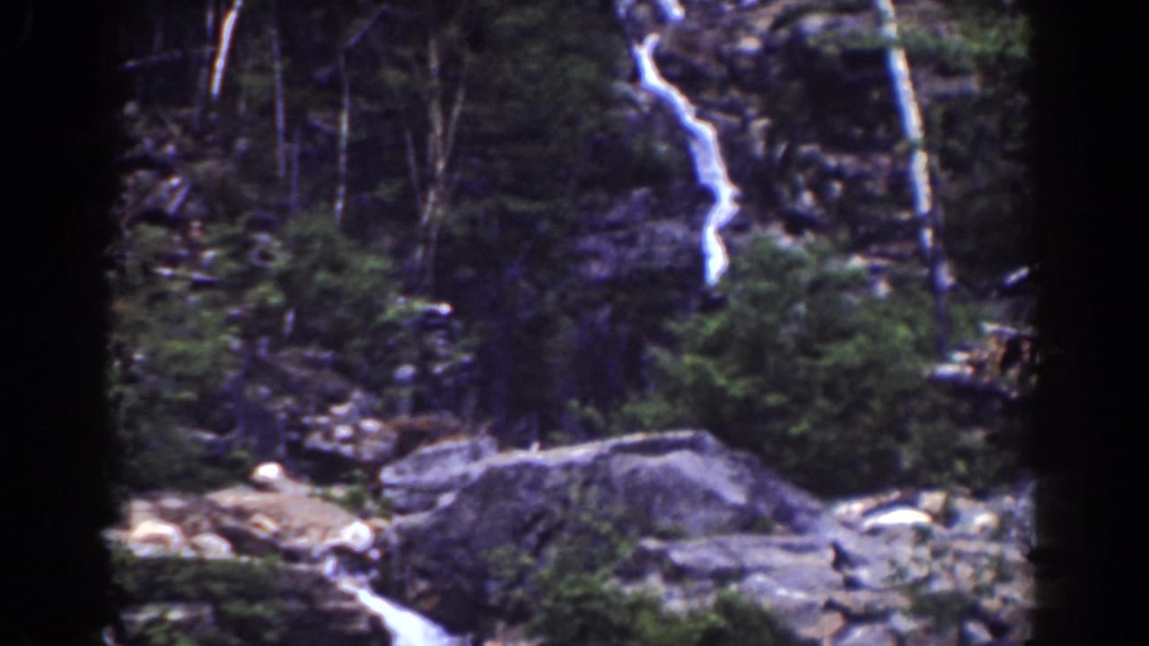 A 1939 8mm view of a distant mountain waterfall, rock face, shrubs, trees, and lower stream area at Mount Washington.