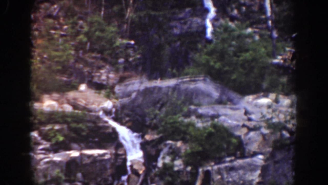 Late-1930s Mount Washington 8mm frame with a bright cascade, large gray boulder, rock ledges, trees, and dense greenery.