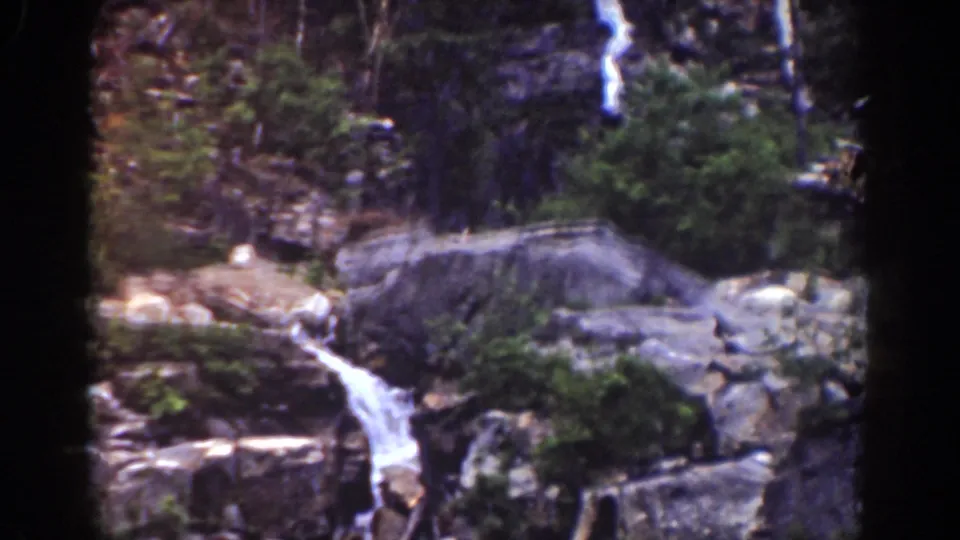 Late-1930s Mount Washington 8mm frame with a bright cascade, large gray boulder, rock ledges, trees, and dense greenery.