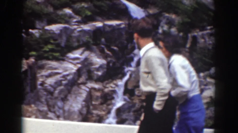 Two adult visitors cross the foreground at a Mount Washington-area waterfall overlook in 1939 8mm footage.