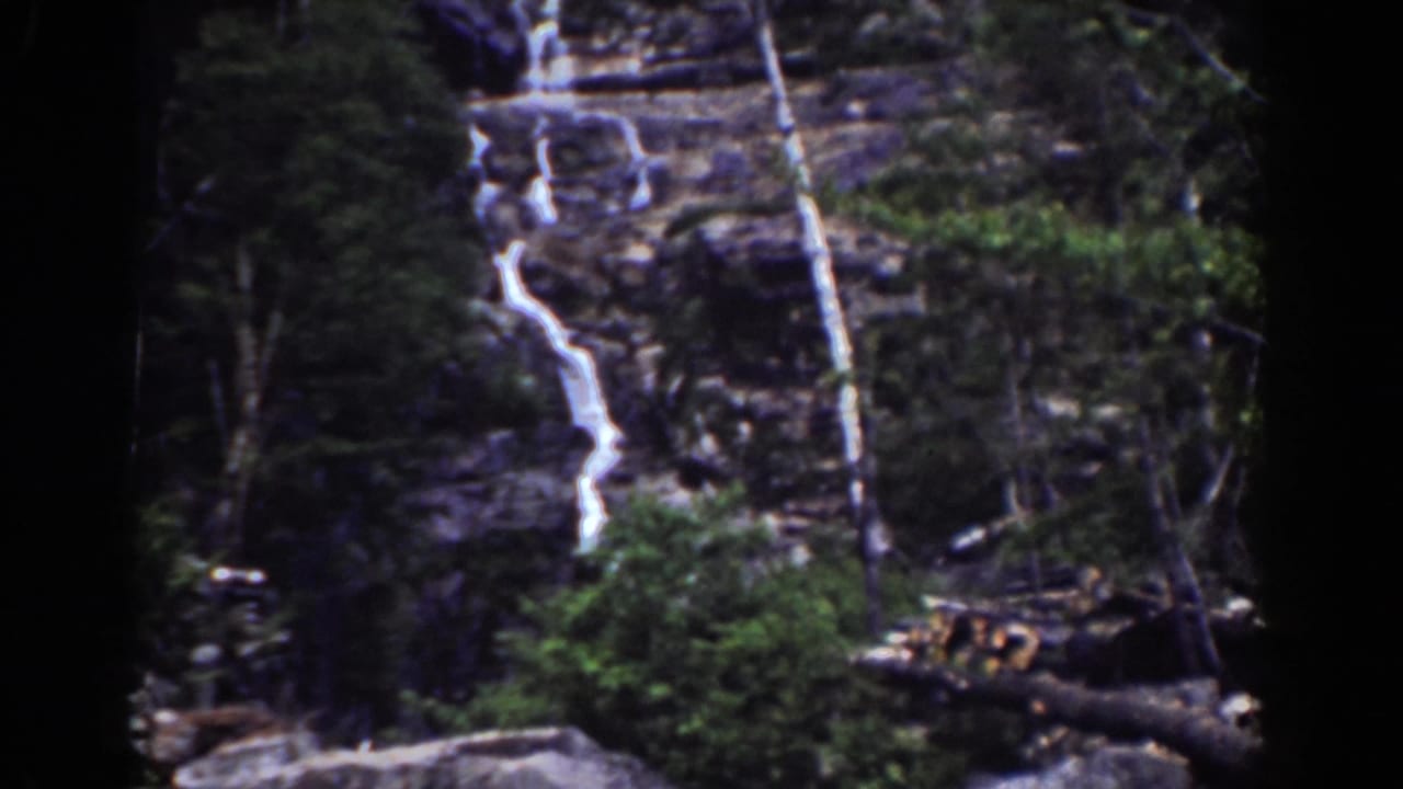 Rocky waterfall descending through trees in a forested mountain setting.