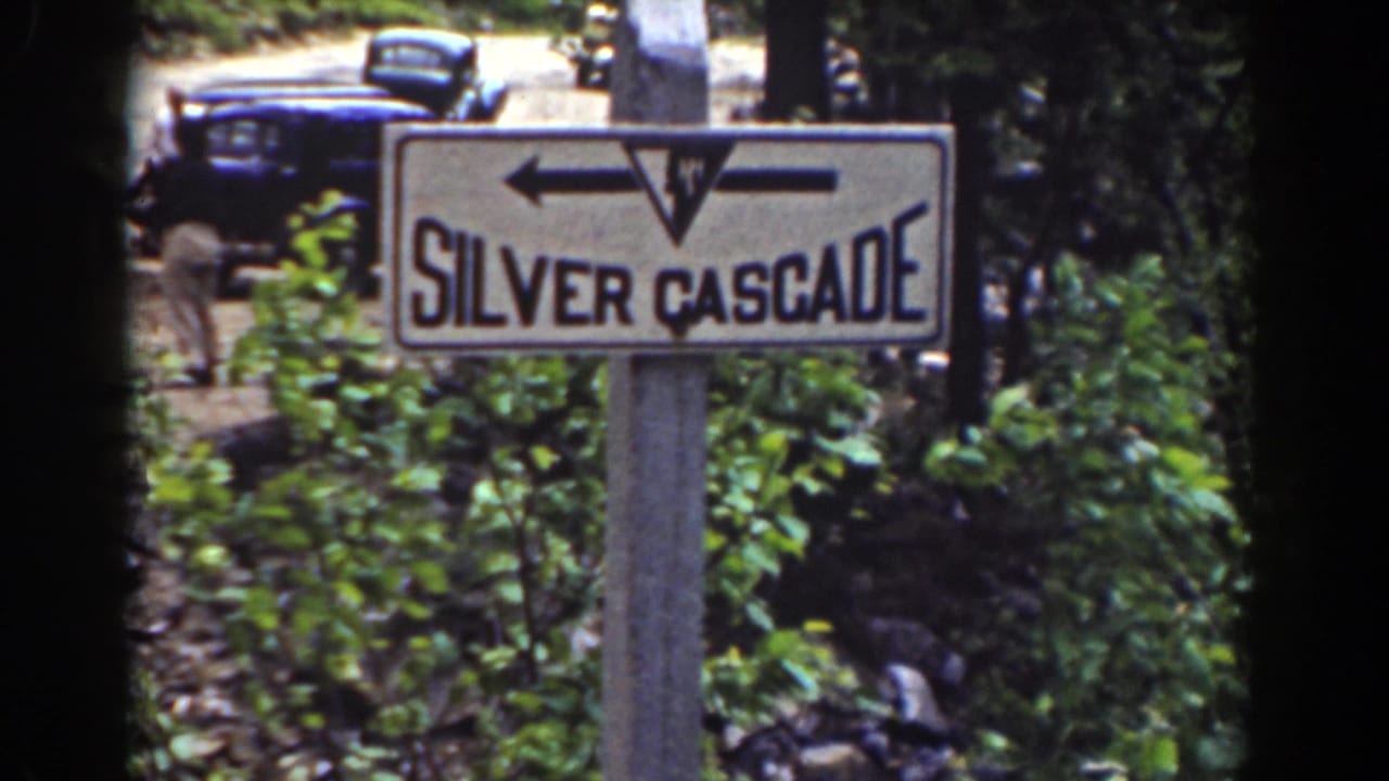 Silver Cascade roadside sign with arrows, foliage, a dark car, and a standing person in the background.
