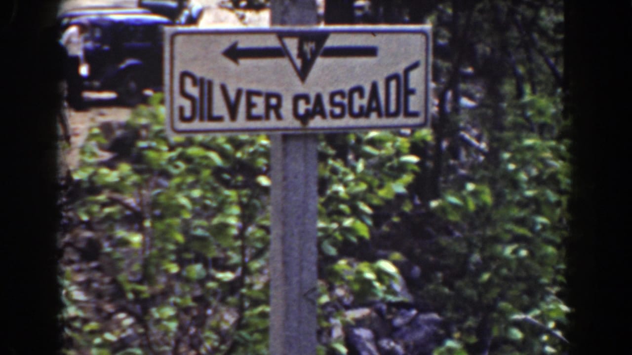 Closer view of the Silver Cascade sign on a post, with trees, shrubs, and a parked car behind it.