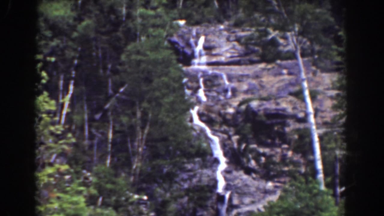 Mount Washington-area home-movie frame showing Silver Cascade dropping over dark rock, with trees and brush around the falls.