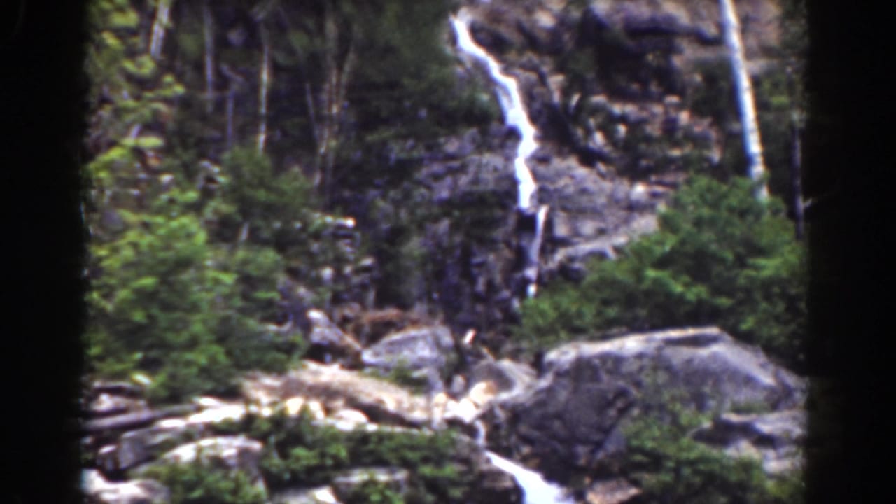 Waterfall drops through rocky forest terrain with dark 8mm frame edges.