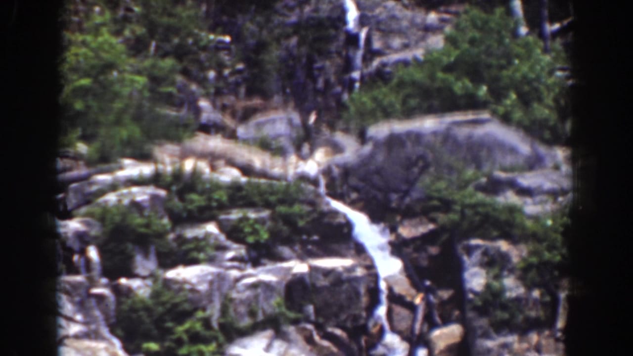 Rocky waterfall channel with trees and dark vertical film gate marks.