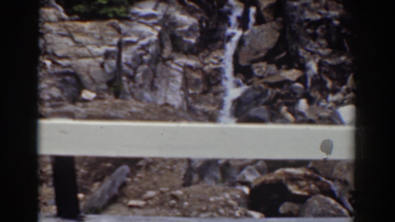 Pale safety rail in front of a narrow waterfall running down rocks.