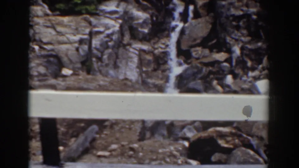 1939 Mount Washington home-movie frame with a pale safety rail before rocky ledges and a narrow falling stream.
