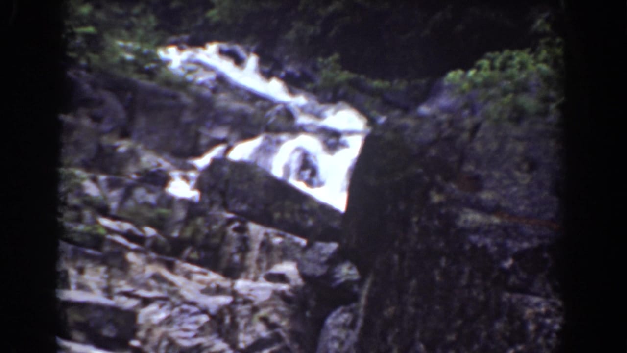 1939 Mount Washington frame showing a bright cascade moving over dark rock formations with trees at the edge.