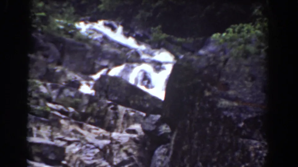 1939 Mount Washington frame showing a bright cascade moving over dark rock formations with trees at the edge.