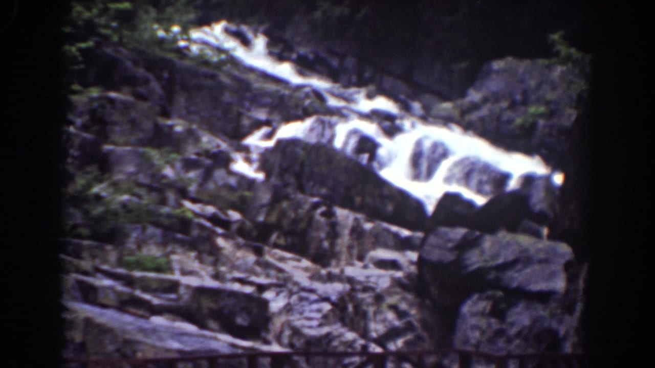 1939 Mount Washington home-movie frame of a broad rocky cascade beside a large foreground boulder and scattered branches.