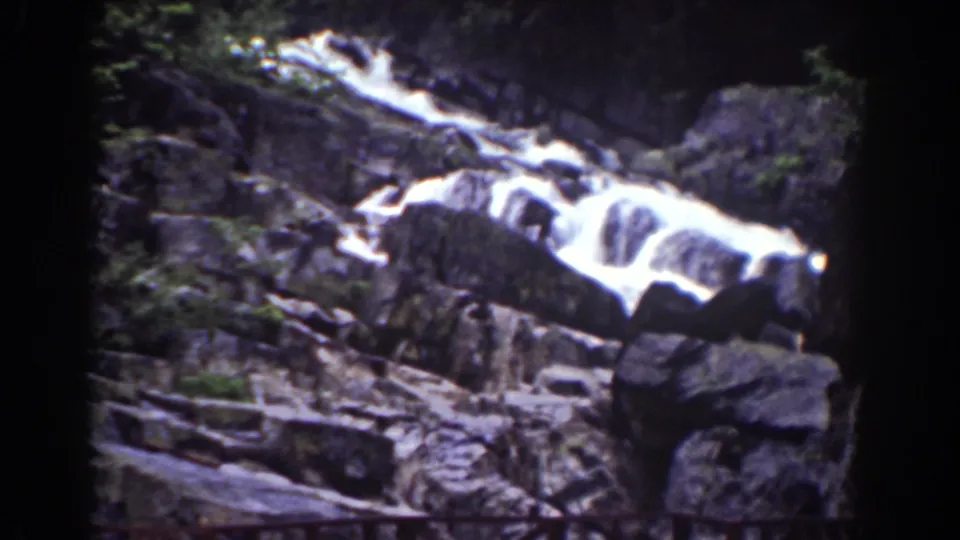 1939 Mount Washington home-movie frame of a broad rocky cascade beside a large foreground boulder and scattered branches.