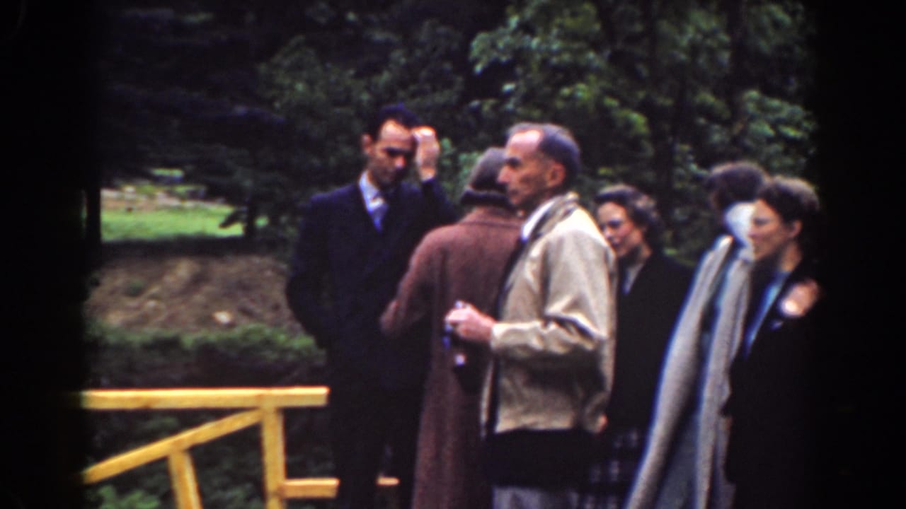 A small group of adults in period coats and suits converse near a yellow wooden railing in Mount Washington, New Hampshire.