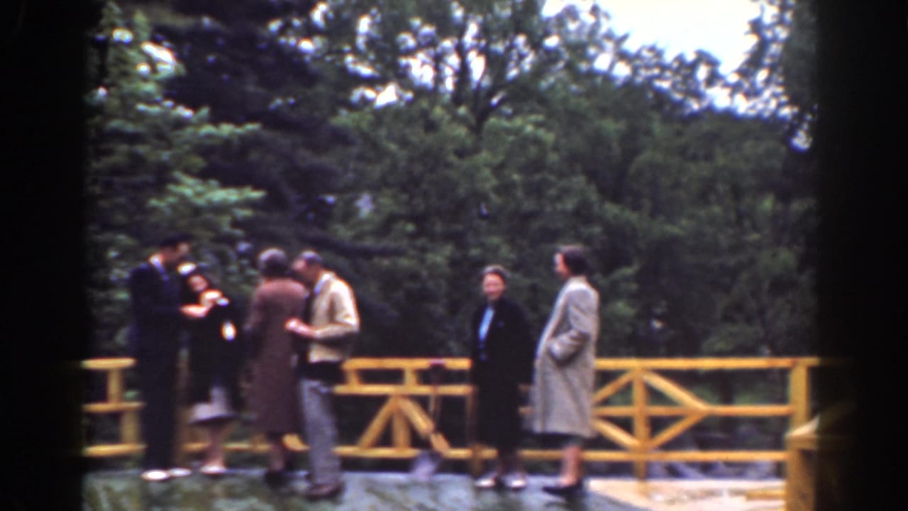 Wide 1939 home-movie view of adults spread across a yellow wooden bridge at a wooded Mount Washington waterfall overlook.