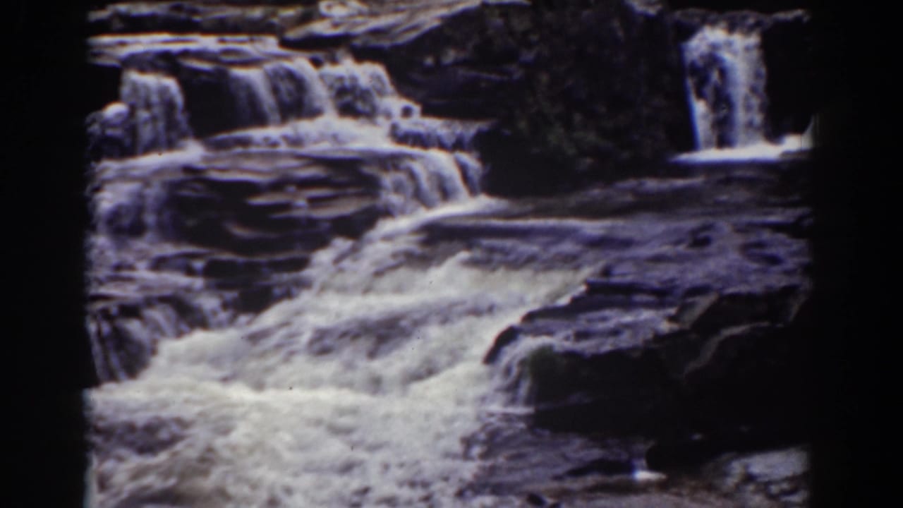 Tiered waterfall flowing over dark rock ledges with white rapids.