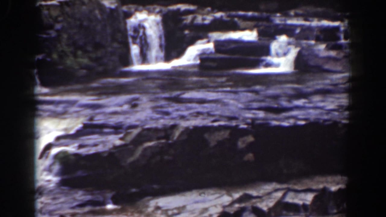 1939 Mount Washington home-movie frame showing a smaller waterfall beyond dark shelves and bright rapids.