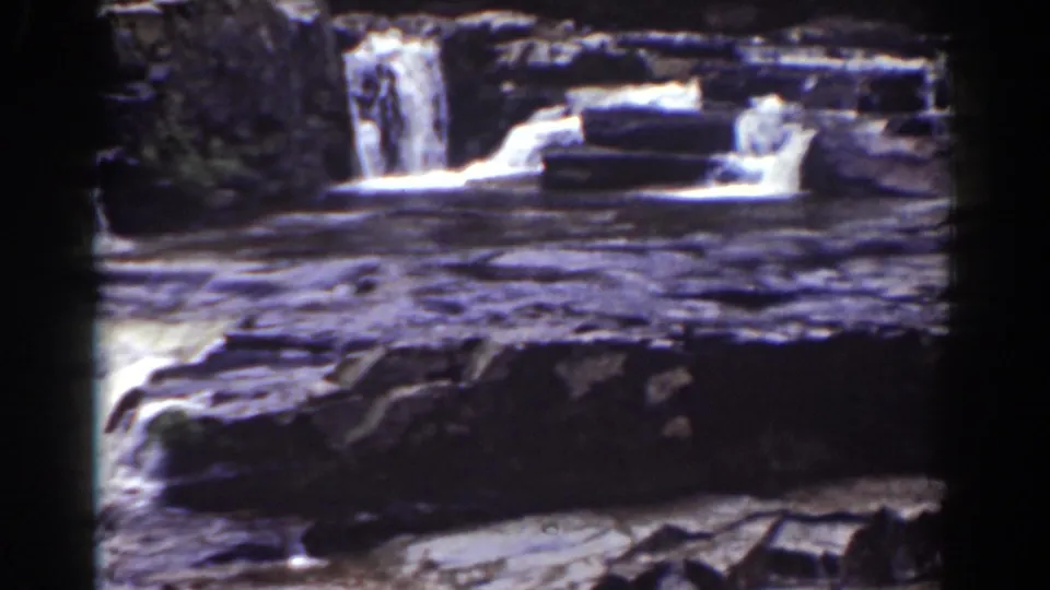 1939 Mount Washington home-movie frame showing a smaller waterfall beyond dark shelves and bright rapids.