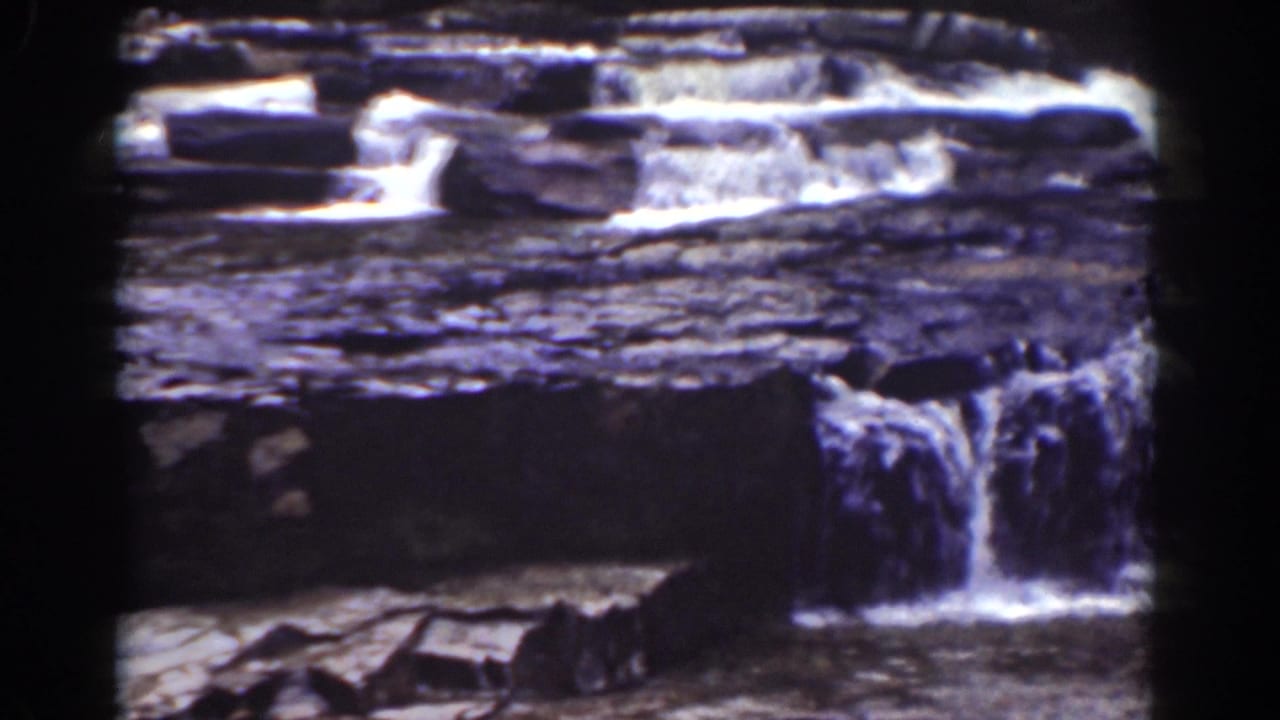 1939 8mm frame of a small cascade dropping from layered stone into a lower, shadowed water channel.