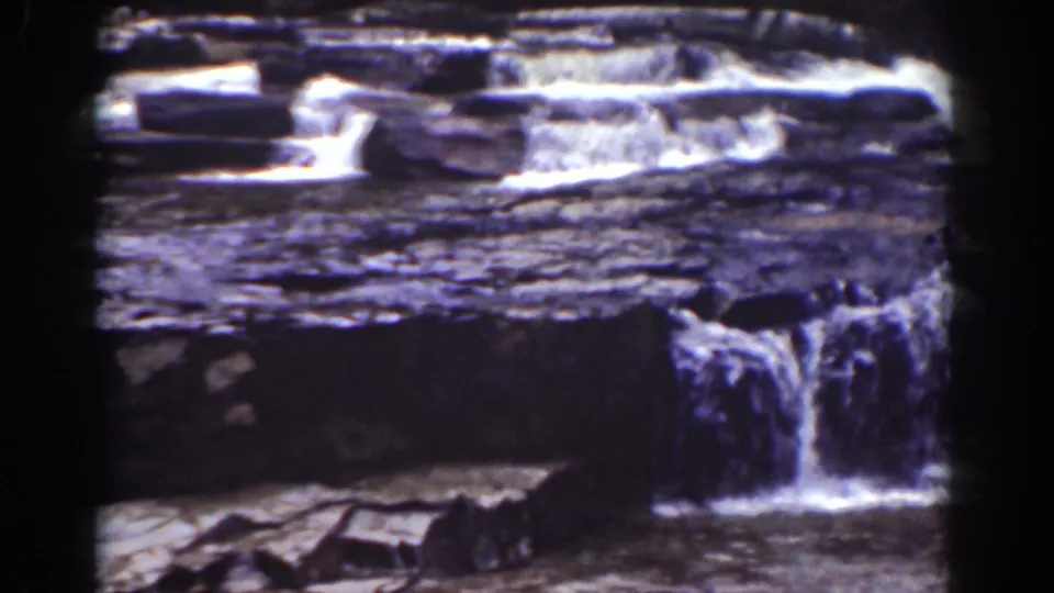 1939 8mm frame of a small cascade dropping from layered stone into a lower, shadowed water channel.