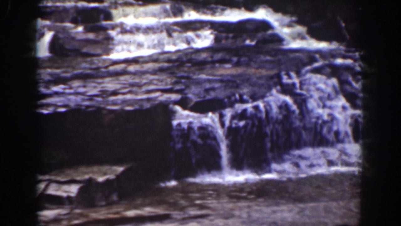 Small waterfall spilling over layered rock ledges into a dark pool.