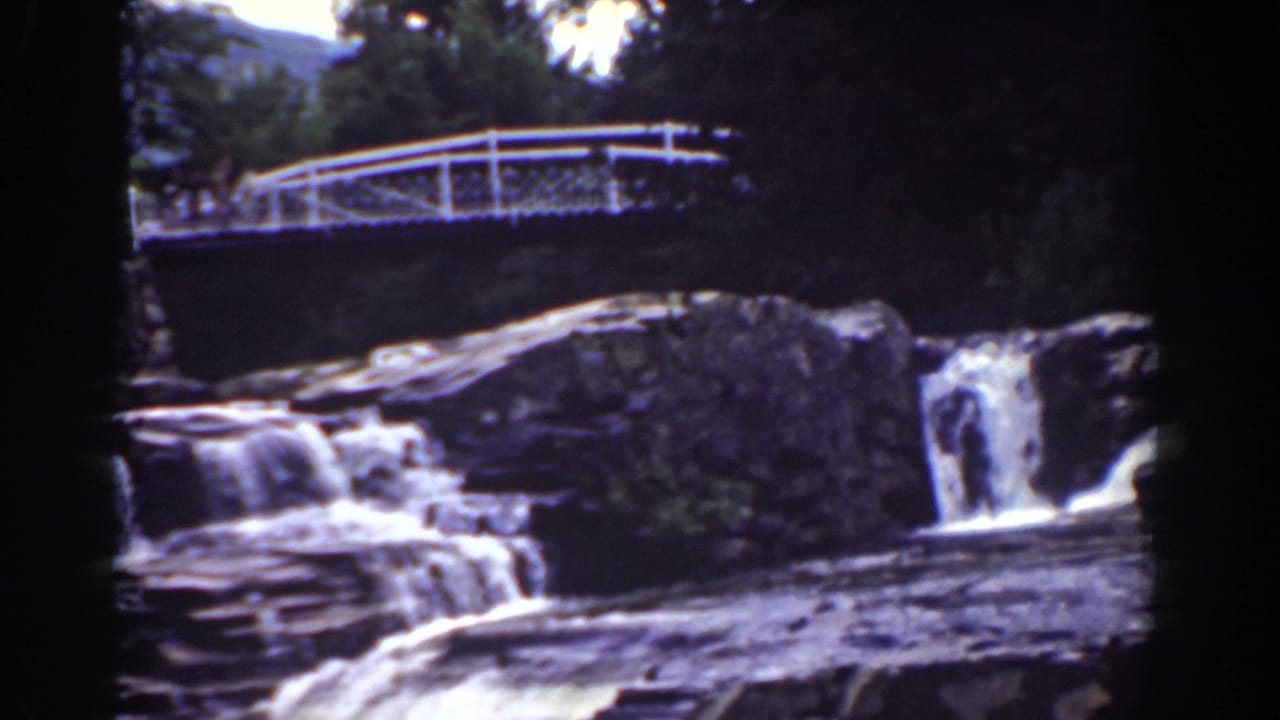 1939 Mount Washington home-movie frame with a white pedestrian bridge crossing above cascades and layered rocks.
