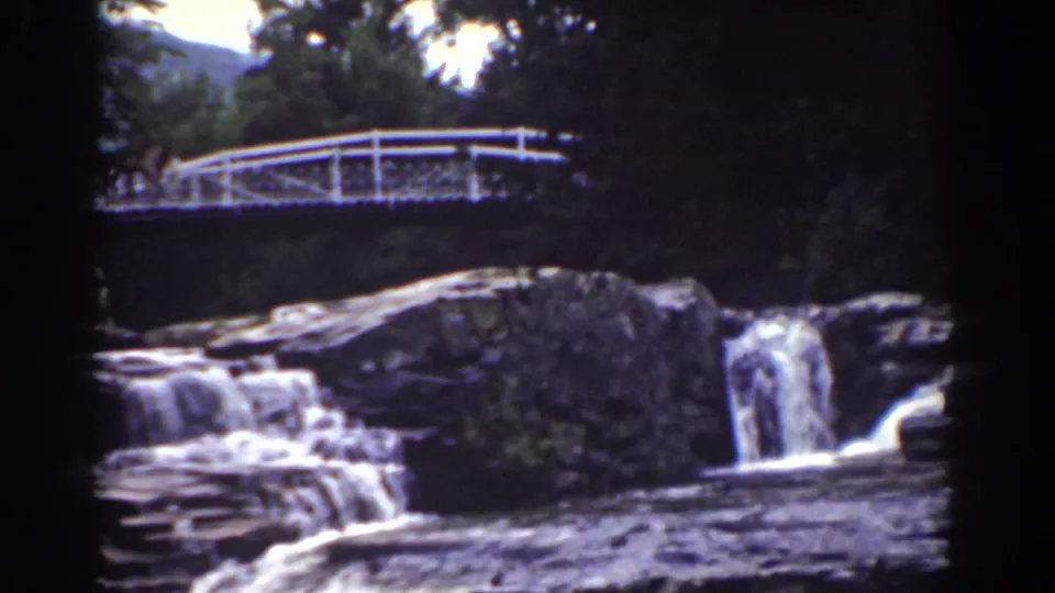 1939 Mount Washington frame showing a white bridge over a rocky cascade, with trees and a faint mountain slope beyond.
