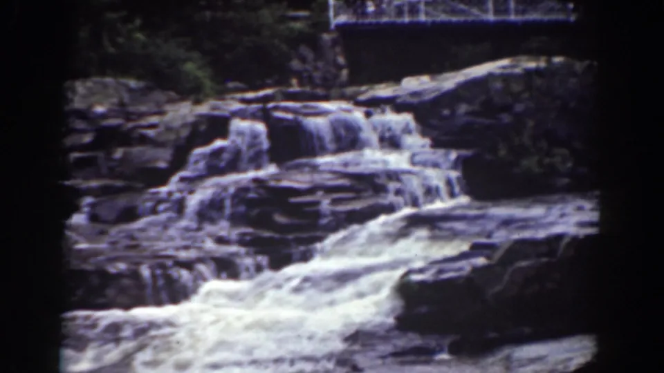 1939 Mount Washington-area 8mm frame showing a rocky waterfall with a white pedestrian bridge above it and dark trees at the edges.