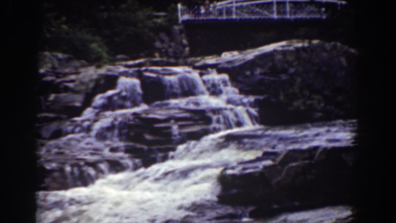 Waterfall and rocky ledges seen beneath a white bridge.