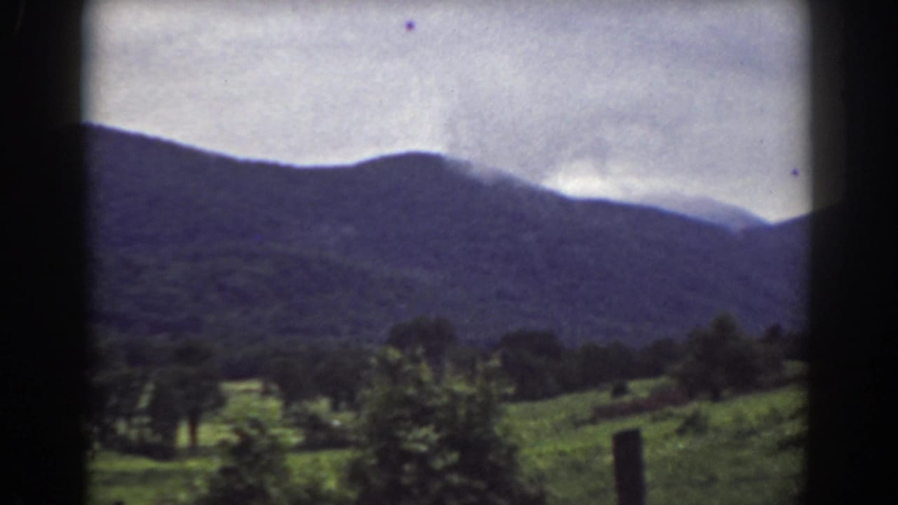1939 Mount Washington-area home-movie view of a green field, trees, and dark mountains under a cloudy sky.