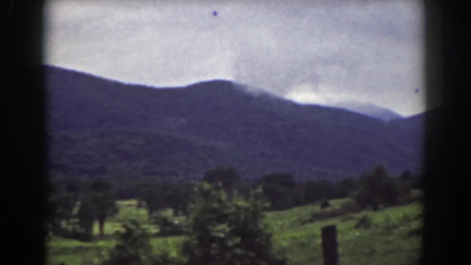 1939 Mount Washington-area home-movie view of a green field, trees, and dark mountains under a cloudy sky.