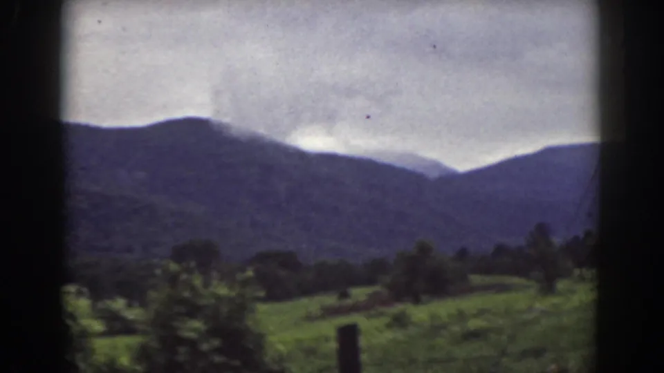 Soft 8mm view of New Hampshire countryside near Mount Washington, with fields and mountains under gray clouds.