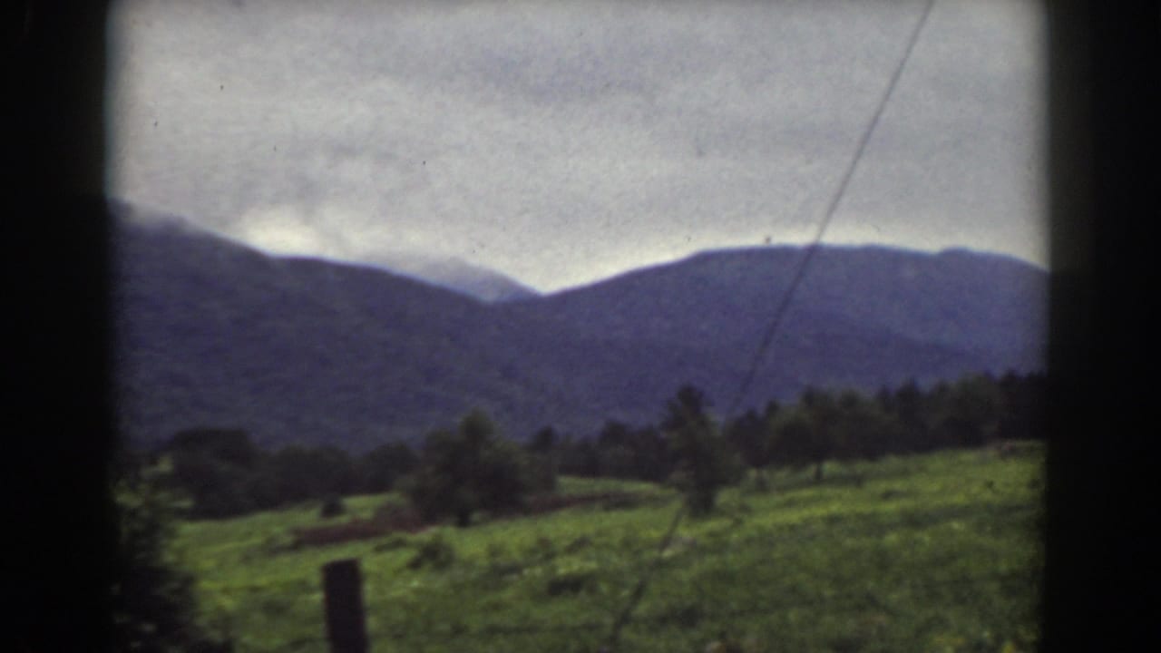 1939 Mount Washington, New Hampshire home-movie frame with a green field, tree line, and layered mountain ridge in soft color.