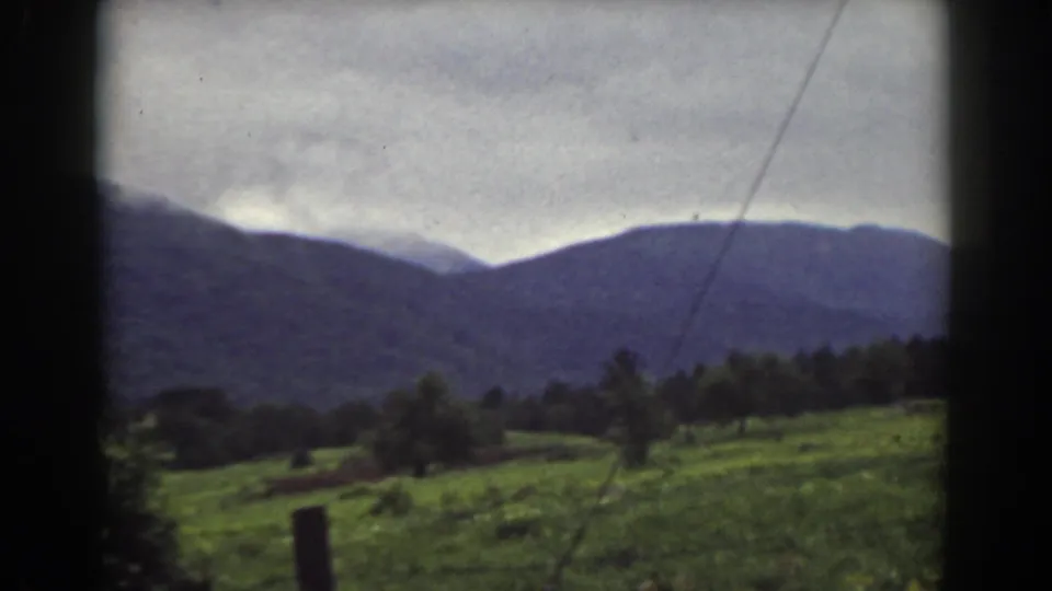 1939 Mount Washington, New Hampshire home-movie frame with a green field, tree line, and layered mountain ridge in soft color.