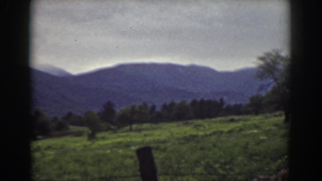 1939 Mount Washington area countryside with a green slope, scattered trees, a foreground fence post, and blue-purple mountain ridges.