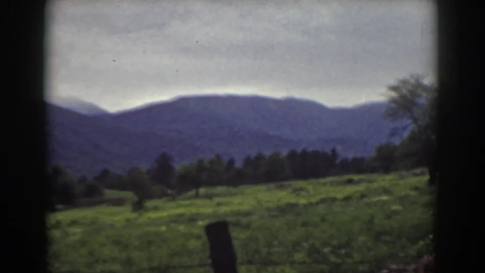 1939 Mount Washington area countryside with a green slope, scattered trees, a foreground fence post, and blue-purple mountain ridges.